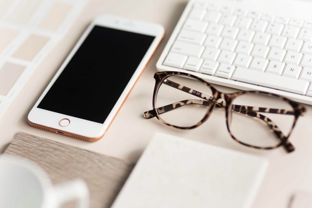 Auf einem Bürotisch liegen ordentlich eine Computerbrille, ein Smartphone, und eine Tastatur.