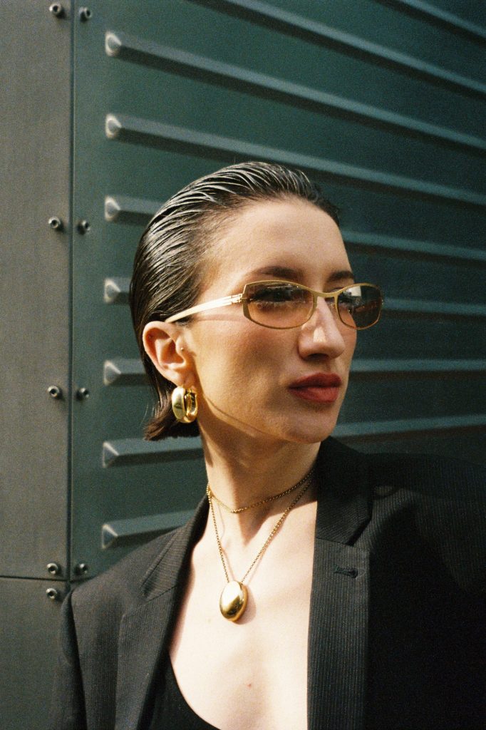 Junge Frau mit nach hinten gelegtem Haar trägt eine elegante Vintage-Sonnenbrille in einer städtischen Umgebung