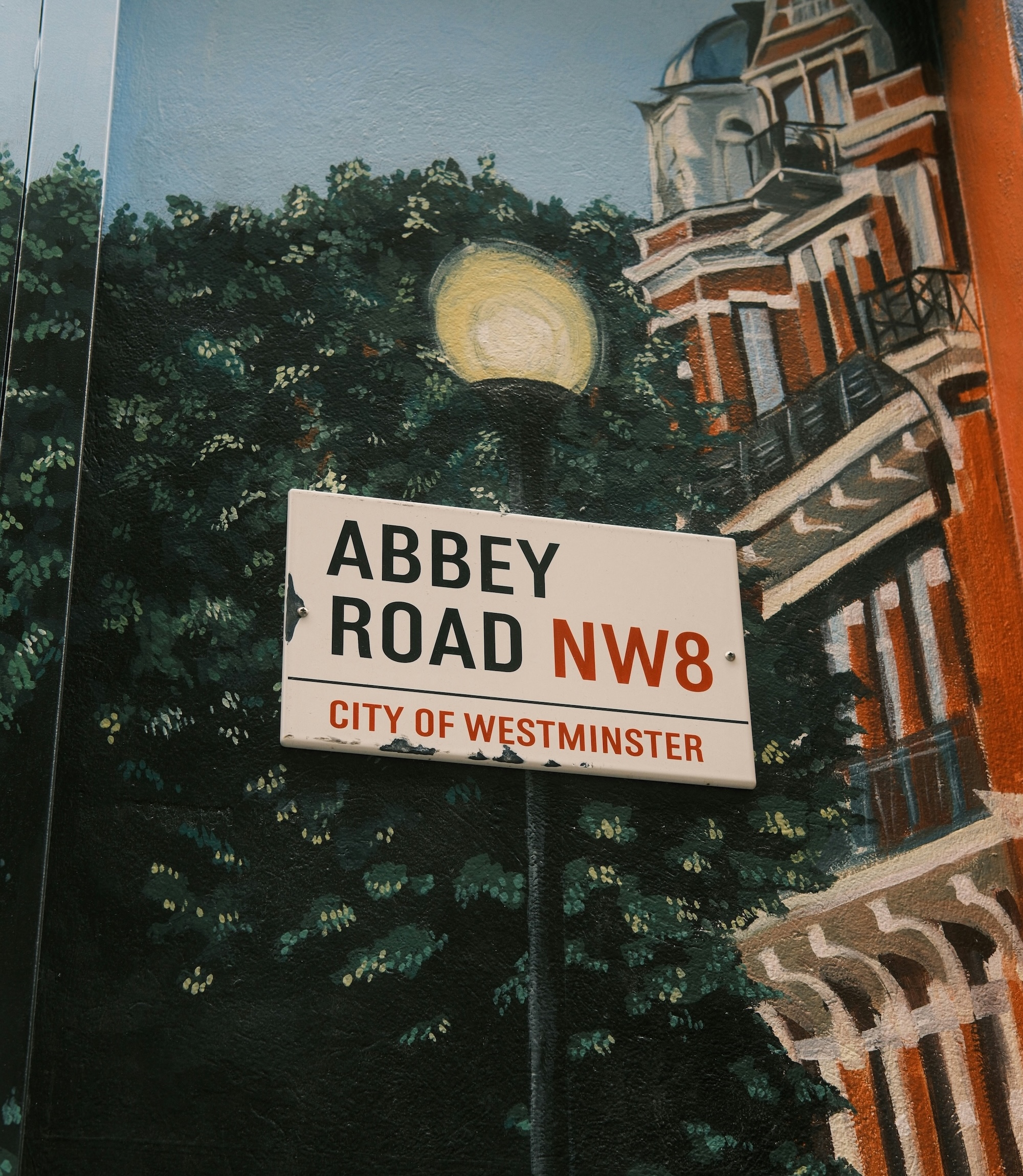 Wandgemälde, das eine Londoner Straßedarstellt. Drauf hängt das Straßenschild „Abbey Road Nw8 City of Westminster”